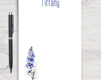 Może przedstawiać: Biały notes z nadrukowanym na górze imieniem "Tiffany". Notes zawiera akwarelowy rysunek fioletowego kwiatu z zielonymi liśćmi w lewym dolnym rogu.