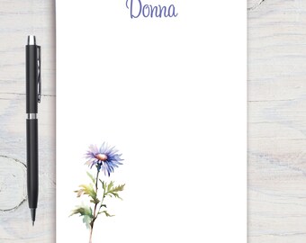 Może przedstawiać: Biały notes z nadrukowanym na górze imieniem "Donna" w kolorze niebieskim. W lewym dolnym rogu znajduje się akwarelowa ilustracja pojedynczego fioletowego kwiatu z zielonymi liśćmi.