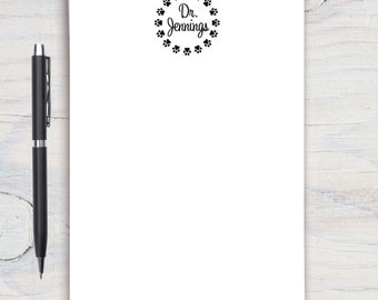 May include: White stationery with a black pen. The stationery features a paw print border around the text "Dr. Jennings" in a script font. The pen is black with silver accents.