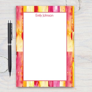 Puede incluir: Un bloc de notas blanco con un borde rojo. El borde está formado por rayas de acuarela en tonos amarillos, naranjas y rosas. El nombre "Emily Johnson" está impreso en rojo en la parte superior del bloc de notas.