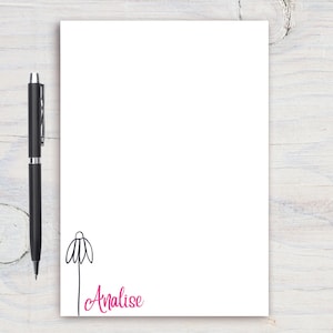 May include: White notepad with a black line drawing of a flower and the name Analise written in pink cursive.
