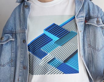 May include: A white t-shirt with a graphic print of a blue and white geometric design. The design is made up of overlapping squares and rectangles.
