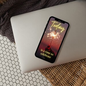 Puede incluir: Un tel&eacute;fono inteligente con una imagen de fondo de puesta de sol rosa y p&uacute;rpura. La pantalla muestra el texto "Today is a time to celebrate" en amarillo con una chispa en primer plano.