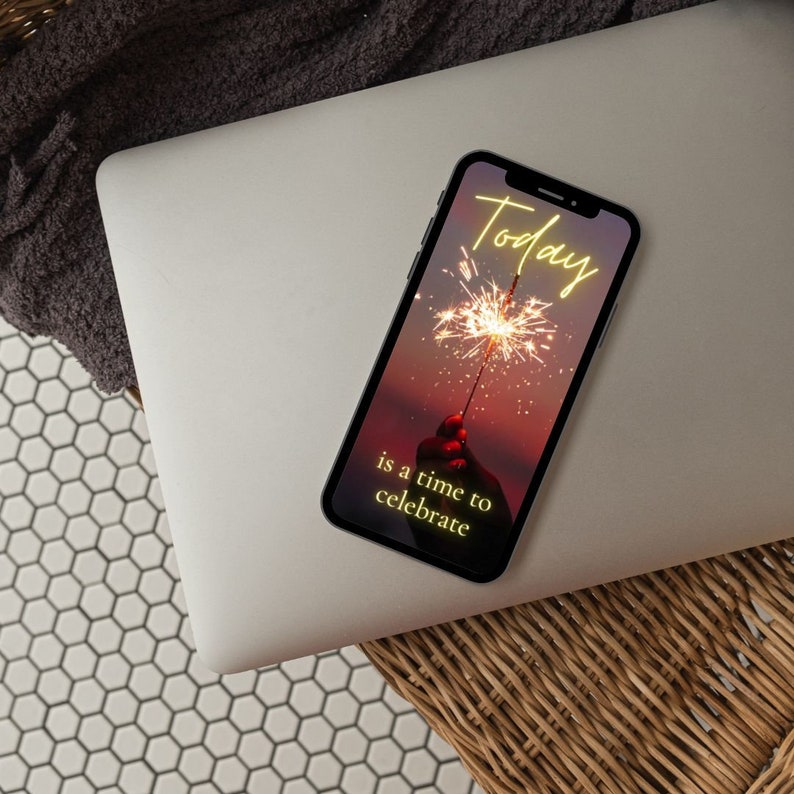Puede incluir: Un tel&eacute;fono inteligente con una imagen de fondo de puesta de sol rosa y p&uacute;rpura. La pantalla muestra el texto "Today is a time to celebrate" en amarillo con una chispa en primer plano.