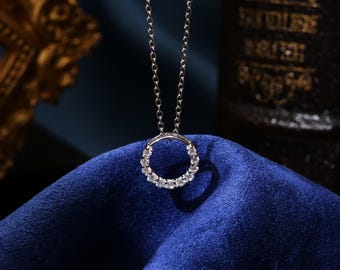 Può includere: Una collana d'argento con un ciondolo rotondo incrostato di piccole pietre trasparenti. La collana è esposta su una superficie di velluto blu.