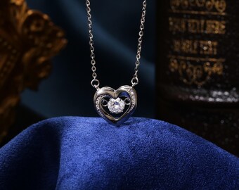 May include: A silver necklace with a heart-shaped pendant featuring a sparkling clear stone in the centre. The heart is open on the sides, revealing the stone.