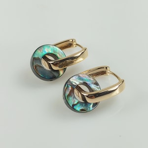 May include: A pair of gold-colored hoop earrings with iridescent abalone shell accents. The earrings feature a circular design with a gold-tone metal clasp. The abalone shell has a mix of green, blue, and purple hues.