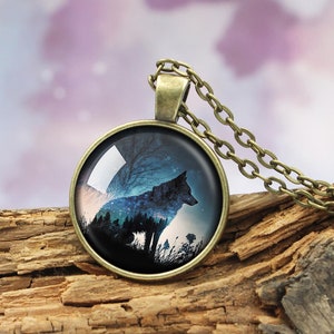 May include: A silver chain necklace with a round glass pendant featuring a silhouette of a wolf howling at the moon against a dark blue and purple starry sky.