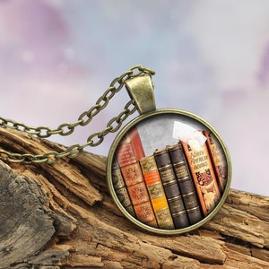 Peut inclure: Un collier en chaîne bronze avec un pendentif rond en verre représentant une pile de livres anciens. Les livres portent des titres comme "North American Indians" et "The Works of Shakespeare".