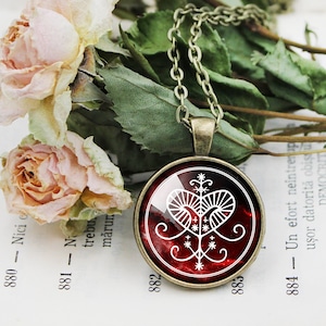 May include: A red glass pendant necklace featuring a white symbol of a heart with a tree inside. The pendant is on a silver chain and is surrounded by a silver frame.