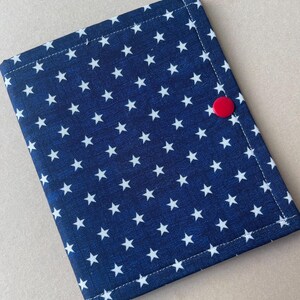 May include: A navy blue fabric item with a white star pattern. The item is rectangular and has a red button closure on the right side. The edges are neatly stitched.