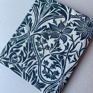 May include: A folded, square fabric item with a button closure. The fabric features a dark teal floral pattern on a white background. The design includes stylized flowers, leaves, and vines, creating a classic, elegant look.