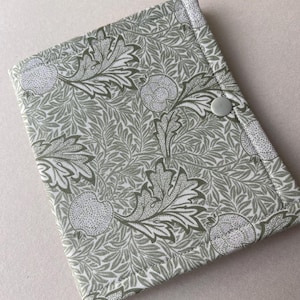 May include: A fabric journal cover with a green and white botanical pattern. The cover features a repeating design of leaves and fruit. A gray button secures the cover closed.