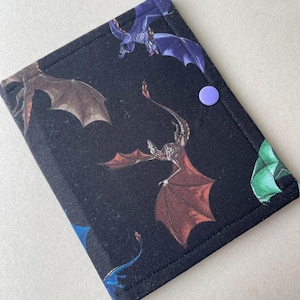 May include: Black fabric book cover featuring a repeating pattern of colorful dragons in shades of red, blue, and green. The cover has a purple snap closure.