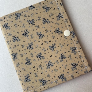May include: A beige fabric notebook cover with a navy blue floral pattern. The cover is rectangular with rounded corners and a white button closure. White stitching outlines the edges.