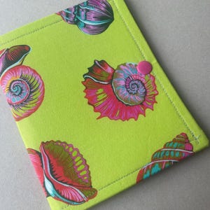 May include: A lime green fabric cover featuring a repeating pattern of colorful seashells in shades of pink, purple, and teal. The rectangular cover is stitched along the edges and includes a single, small, solid pink circular snap button closure.