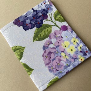 May include: A fabric case featuring a floral hydrangea design in shades of purple, lavender, and yellow, with green leaves. The case has a white background with a subtle swirl pattern and a purple button closure.