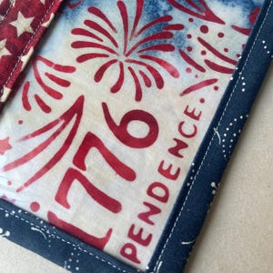 May include: Close-up of a patriotic fabric item with a red, white, and blue color scheme. The design features fireworks, the number "1776", and the word "INDEPENDENCE". The item is trimmed with a dark blue fabric with white dots and a red and white star pattern.