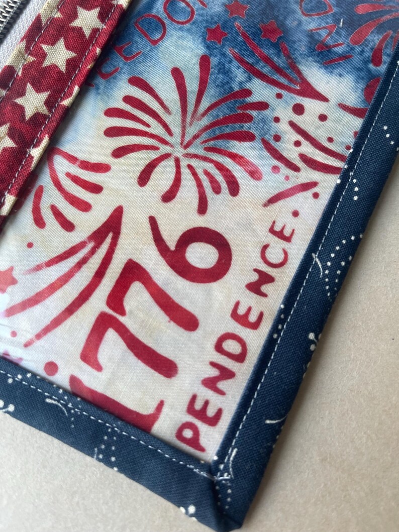 May include: Close-up of a patriotic fabric item with a red, white, and blue color scheme. The design features fireworks, the number "1776", and the word "INDEPENDENCE". The item is trimmed with a dark blue fabric with white dots and a red and white star pattern.