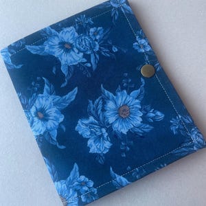 May include: A navy blue floral fabric cover with a repeating pattern of light blue flowers and leaves. The cover is rectangular with a brass snap closure and white stitching around the edges. The overall design is a botanical theme.