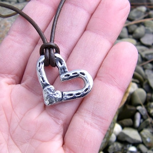 May include: A silver heart-shaped pendant made from a horseshoe, hanging from a brown leather cord.