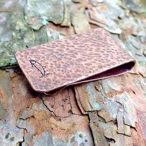 May include: A hammered copper money clip with a small fish design engraved on the front.