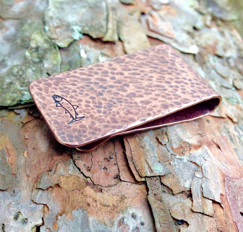 May include: A hammered copper money clip with a small fish design engraved on the front.
