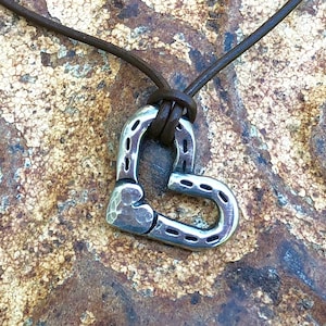 May include: A silver horseshoe shaped heart pendant on a brown leather cord necklace.