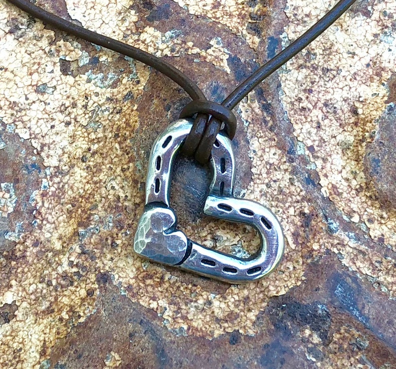 May include: A silver horseshoe shaped heart pendant on a brown leather cord necklace.