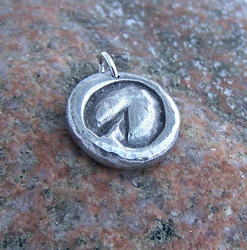May include: A silver pendant with a hammered finish and a circular design featuring a stylized arrow pointing upwards.