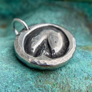 May include: A silver charm in the shape of a horseshoe, with a hammered texture. The charm has a loop for attaching to a necklace or bracelet.