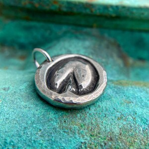 May include: Silver charm with a hammered finish and a raised horseshoe design. The charm has a loop for attaching to a necklace or bracelet.