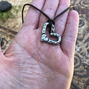 May include: A silver heart-shaped pendant necklace with a hammered texture, hanging from a brown leather cord.
