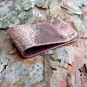 May include: A hammered copper money clip with a slightly curved design. The clip has a textured surface and a smooth, rounded edge.