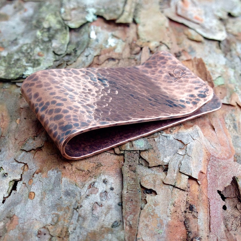 May include: A hammered copper money clip with a slightly curved design. The clip has a textured surface and a smooth, rounded edge.