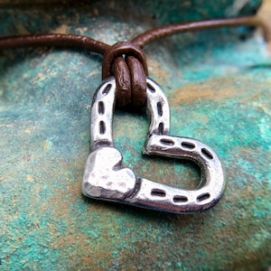 May include: A silver heart-shaped pendant necklace with a horseshoe design. The necklace is made of brown leather cord.