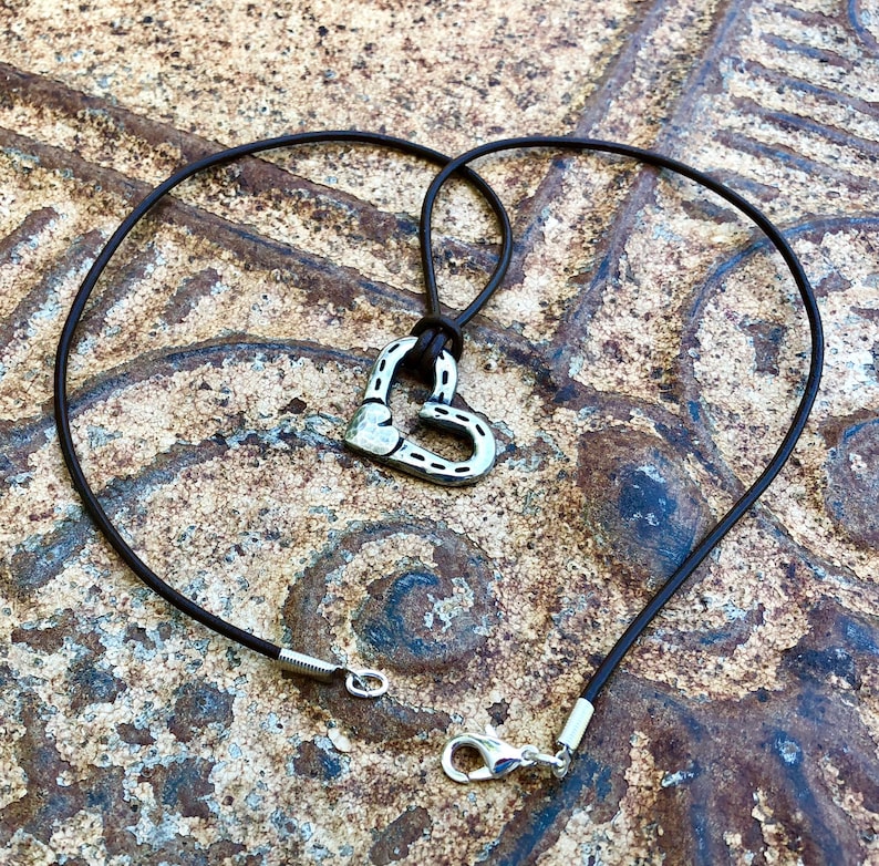 May include: A brown leather cord necklace with a silver horseshoe heart pendant.