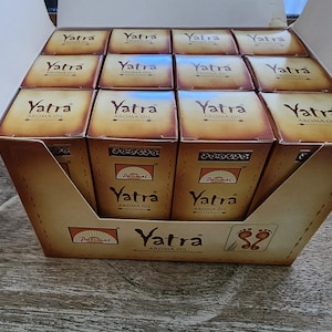 May include: A display box containing multiple small boxes of Yatra Aroma Oil. The boxes are brown with the word "Yatra" and "Aroma Oil" printed on them. The Parimal logo is also visible.