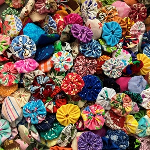 May include: A collection of colorful fabric rosettes, also known as cinched rosettes, in various patterns and designs. The rosettes are made from different fabrics, including floral prints, polka dots, and geometric patterns.