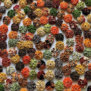 May include: A collection of numerous fabric yo-yos arranged in a spiral pattern. The circular fabric pieces feature a variety of colors including orange, yellow, brown, green, and black, with various floral, polka dot, and solid patterns.