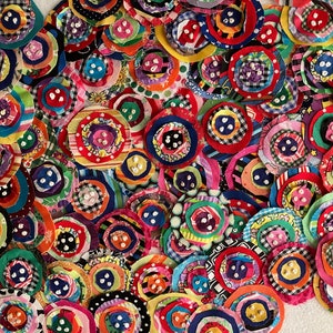 May include: A collection of colorful, handmade fabric circles with button centers. The circles feature various patterns and colors, including red, blue, yellow, and green. Some have three buttons, while others have five. These could be used for crafts.