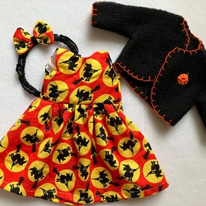 May include: A sleeveless dress featuring a red background with yellow circles and black silhouettes of witches on broomsticks, a matching headband with a bow, and a black long-sleeve jacket with orange blanket stitching and a small orange pumpkin.