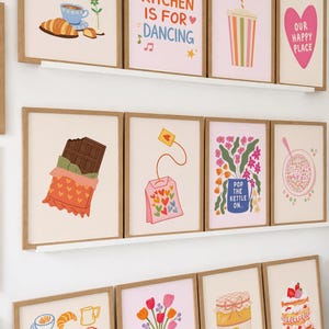 May include: A collection of framed art prints with a kitchen theme. The prints feature illustrations of food, drinks, and phrases like "Bon Appetit" and "This Kitchen is for Dancing." The color palette includes pastels and warm tones.