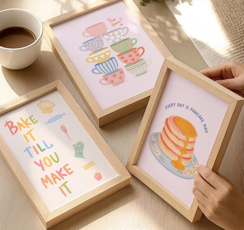 May include: Three framed art prints with light wood frames. One print says "Bake it till you make it" with baking-themed illustrations. Another shows stacked teacups and the text "Tea time?". The third says "Every day is pancake day".