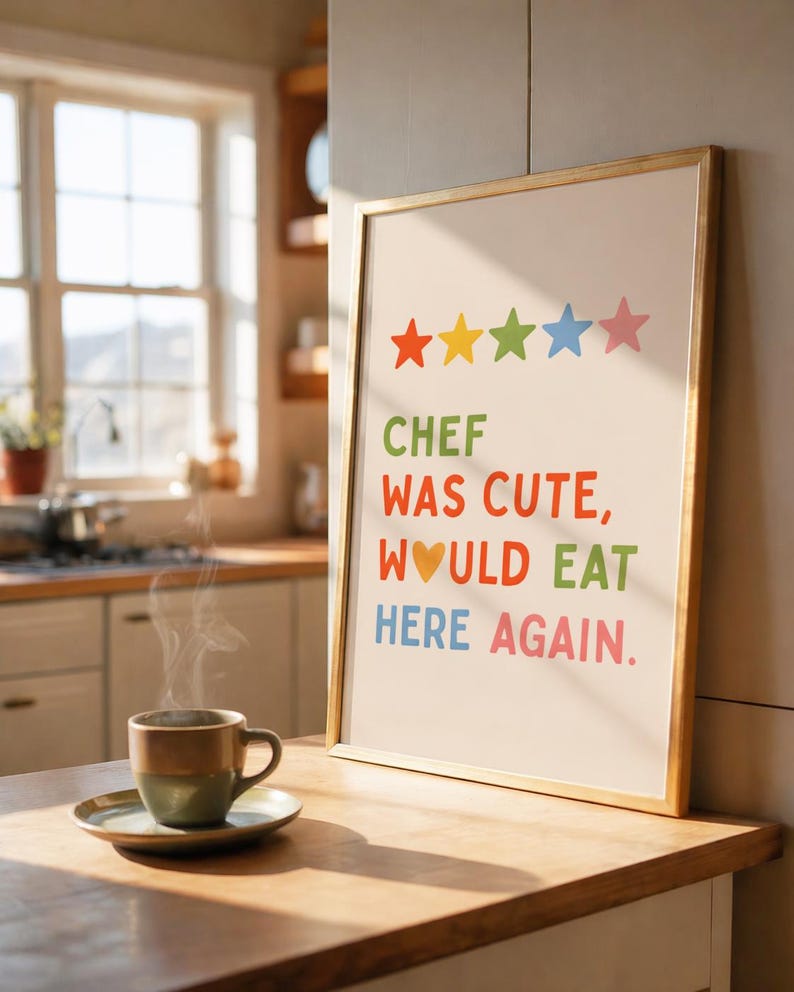May include: A framed print with the text "CHEF WAS CUTE, WOULD EAT HERE AGAIN" in colorful letters. Above the text are five stars in orange, yellow, green, blue, and pink. A cup of coffee sits on a saucer in the foreground.