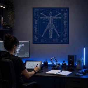 Könnte beinhalten: Ein dunkelblauer Druck des Vitruvianischen Menschen, eine Darstellung des menschlichen Körpers, hängt an einer Wand. Eine Person arbeitet an einem Schreibtisch mit Computer, Tablet und Robotermodellen. Der Raum wird durch blaue Akzentbeleuchtung beleuchtet.