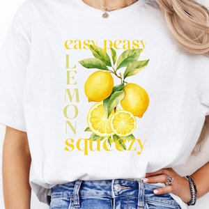 May include: White t-shirt featuring a watercolor illustration of lemons with green leaves. The text "easy peasy lemon squeezy" is printed in yellow. The shirt is paired with blue jeans.