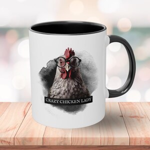 Puede incluir: Taza de cerámica blanca con borde y asa negros. La taza presenta un gráfico de una gallina con gafas redondas y el texto "Crazy Chicken Lady".