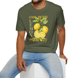May include: Olive green t-shirt with a watercolor illustration of lemons and leaves. The text "easy peasy lemon squeezy" is printed in yellow. The shirt is short-sleeved and has a crew neck.