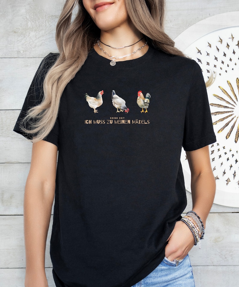 May include: Black t-shirt featuring a graphic of three chickens and a rooster. The text "Keine Zeit Ich Muss Zu Meinen M&auml;dels" is printed below the graphic.